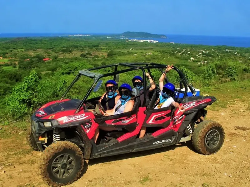 Four guests in a red four-seat RZR on a hilltop with the Punta de Mita coastline behind