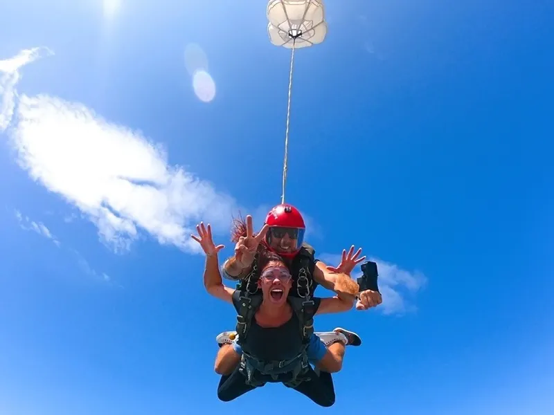 Instructor and guest in free fall with a drogue chute above them against a blue sky