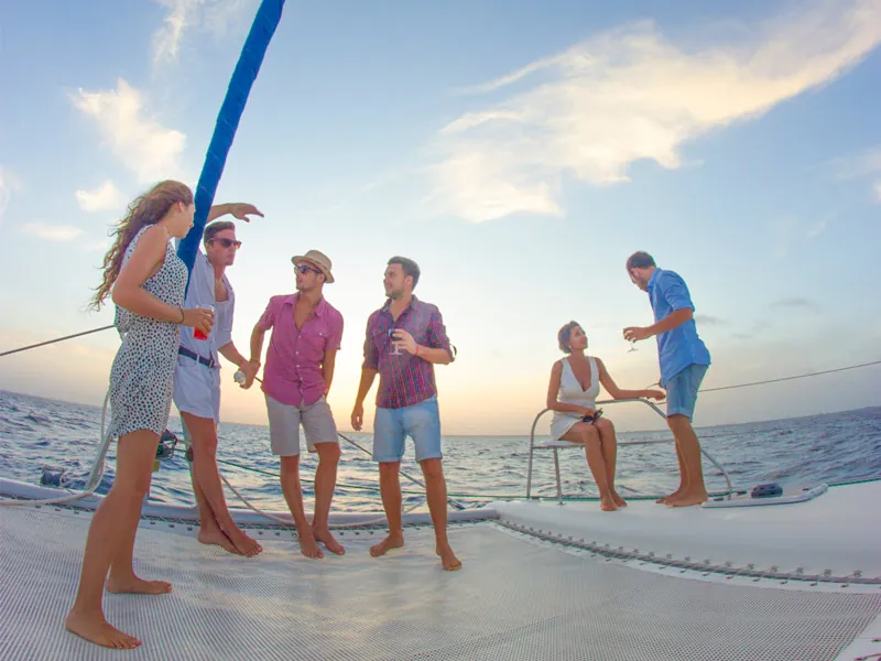 A group of friends with drinks standing on the deck of a sailing catamaran in evening light