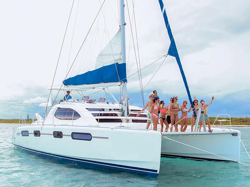 Guests waving from the bow of a Leopard 46 sailing catamaran in shallow turquoise water