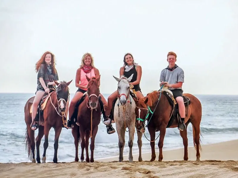 Four guests on horseback posing on the beach by the sea