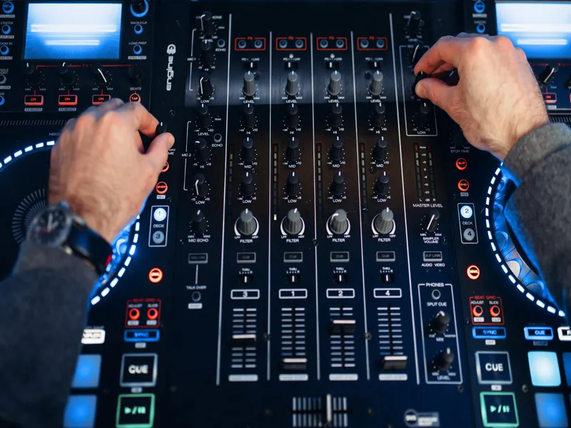 Hands on a lit DJ controller and mixer