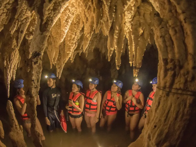 Swimmers in helmets with headlamps and life jackets standing among stalactites in a cave