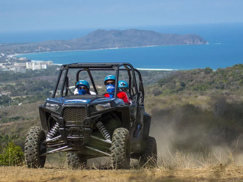 Black four-seat RZR buggy on a hilltop with the Riviera Nayarit coast and a headland behind