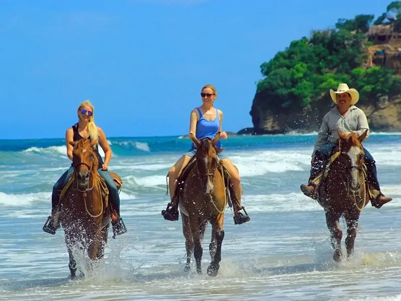 Horses in the surf at Punta de Mita Three riders walking their horses through the surf on a beach at Punta de Mita, green headland behind