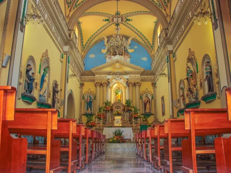 Nave of the Talpa basilica with painted vaults, gilded altar and rows of wooden pews