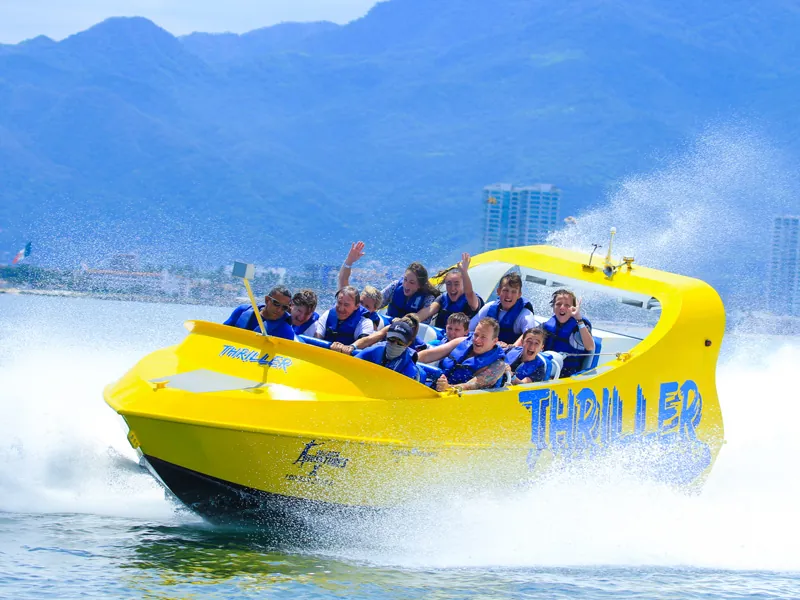 Yellow Thriller jet boat leaning through a turn with passengers in blue vests, Puerto Vallarta behind