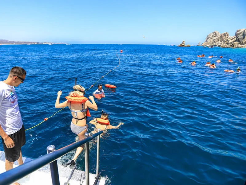 Guest in a life vest climbing down the catamaran ladder toward snorkelers in the sea