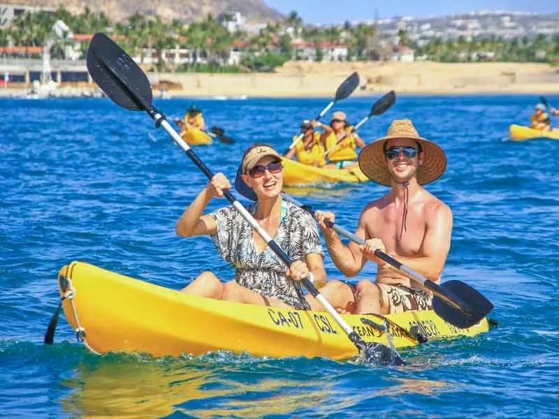 Couple in sun hats paddling a yellow kayak in the bay of Cabo San Lucas