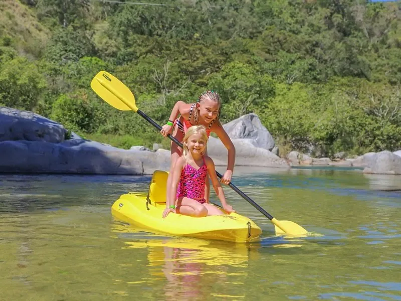 Two girls paddling a yellow kayak in a natural river pool between granite boulders