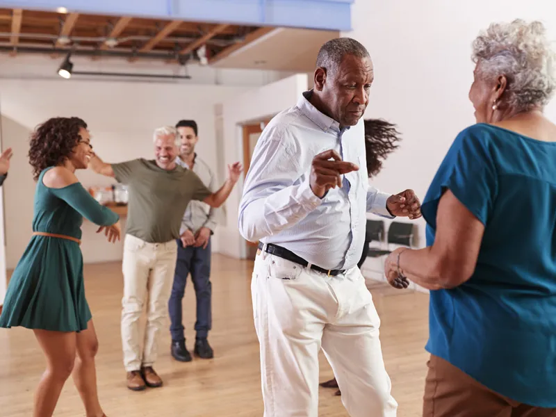 Older couple dancing salsa with other pairs behind them in a sunlit studio