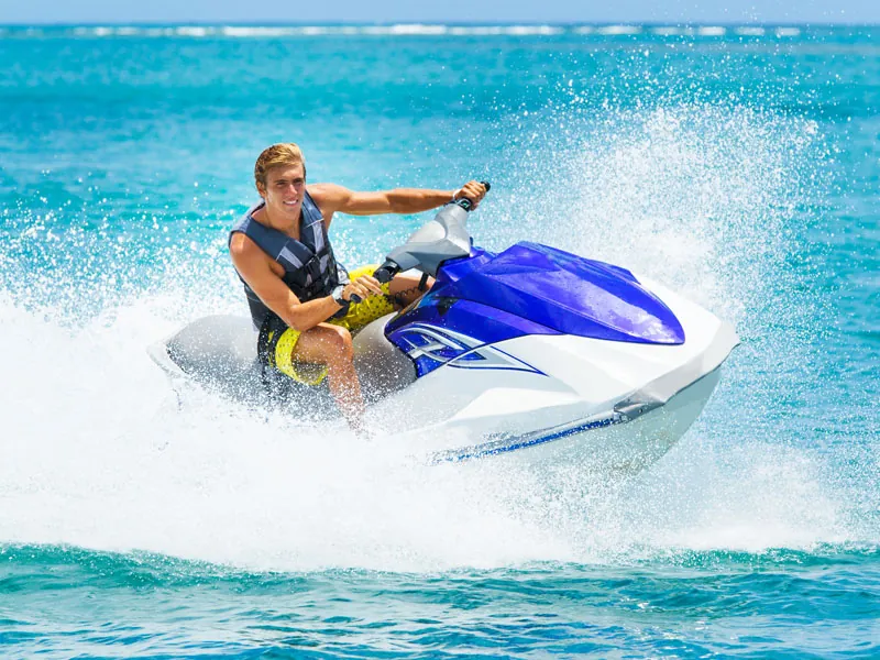 Rider leaning into a turn on a blue and white jet ski, spray flying over turquoise water