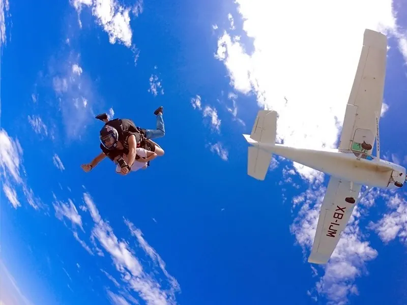 Tandem pair tumbling away from a small white plane high above the clouds