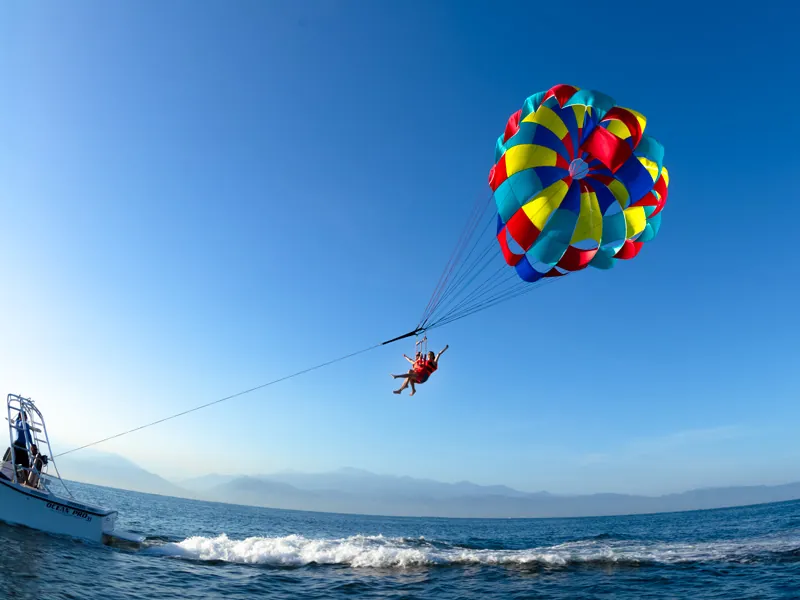 Multicolored parasail canopy lifting a rider from a boat over Banderas Bay, mountains behind
