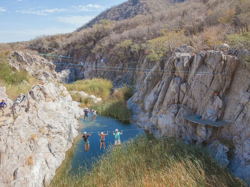 Zip-line cables stretched across a rocky canyon with a pool below