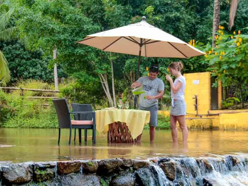 Couple standing beside a lunch table set in a shallow river under a sun umbrella