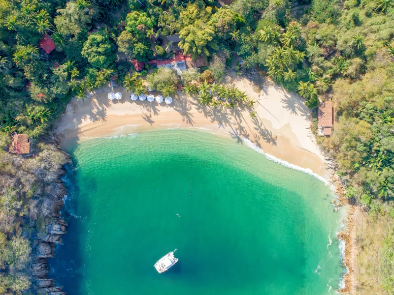 Aerial view of Majahuitas cove with a yacht anchored in green water below a sand beach and jungle