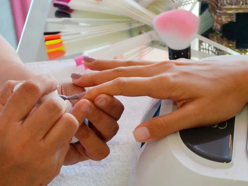 Manicurist shaping a guest’s nails at a table with polish bottles behind