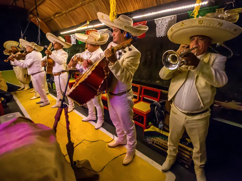 Mariachi musicians in white charro suits and sombreros play aboard a trajinera at night