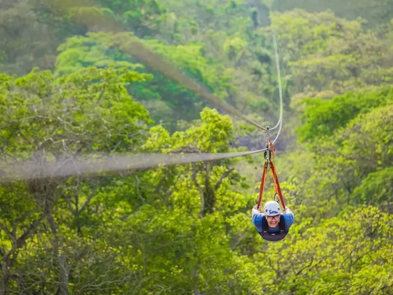 Guest on a long zip line stretching across a forested valley near Puerto Vallarta