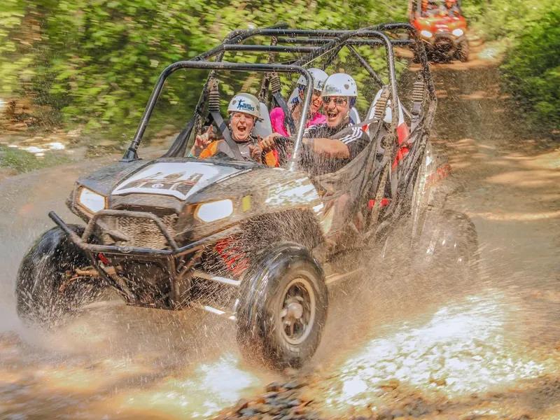 Guests waving from an all-terrain vehicle on a muddy jungle track