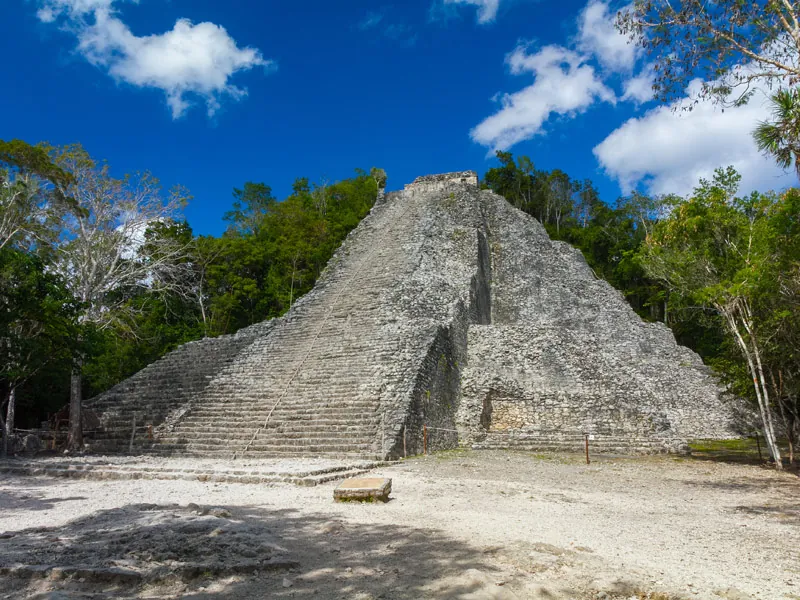 The tall stepped pyramid of Nohoch Mul at Cobá rising above the forest under a blue sky