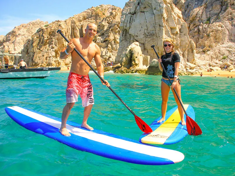 Two guests on paddleboards in turquoise water below the granite rocks of Land’s End