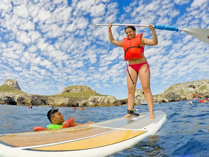 Guest standing on a paddleboard with her paddle raised, Marietas Islands behind