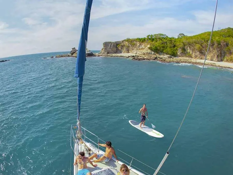 Paddleboarder in a green cove seen from the bow of a sailboat