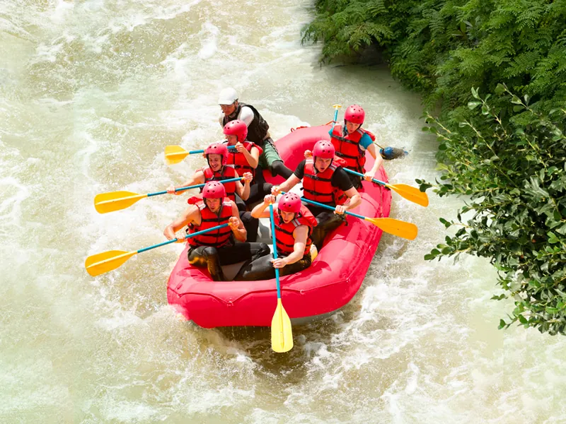 A group in red helmets and life vests paddles an inflatable raft through white water