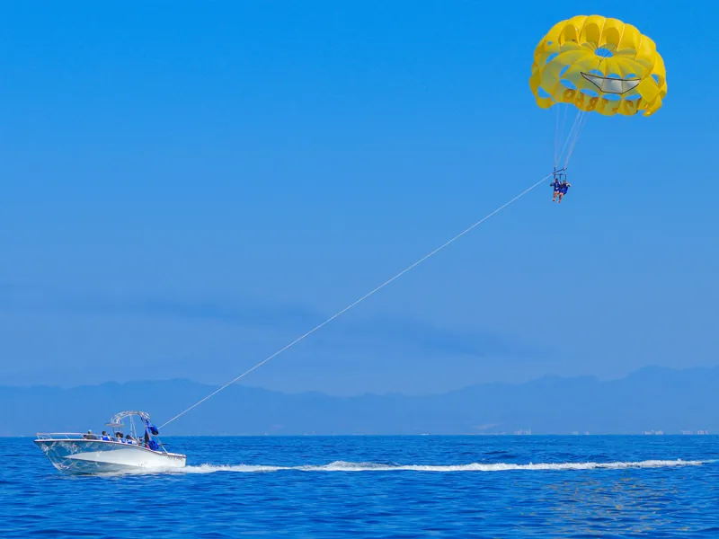 Yellow parasail canopy high above Banderas Bay, towed by a boat with mountains on the horizon