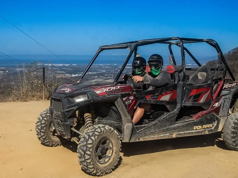 Two guests in bandanas in a red RZR parked on a dirt road high above Banderas Bay