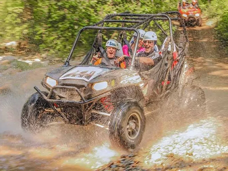 Guests in helmets driving a Polaris UTV through a muddy jungle track