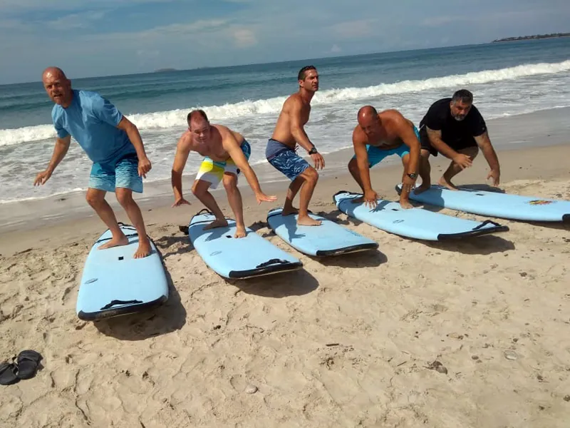 Five students practicing pop-ups on soft-top surfboards laid on the sand