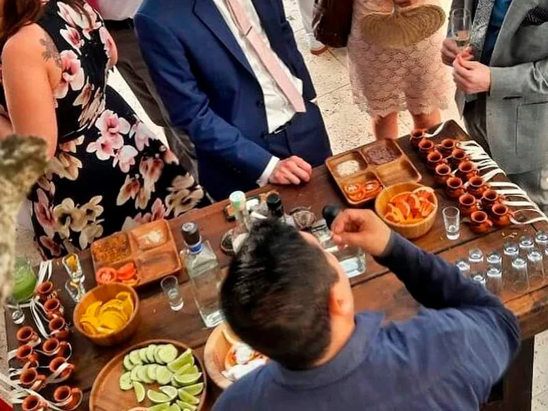 Host pouring at a wooden table of clay cups, limes, oranges and salts for guests at an event