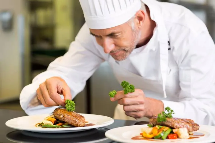 Private chef finishing plates Chef in whites garnishing plates of steak and vegetables