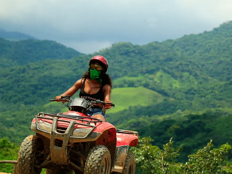 Woman in a helmet and bandana riding a red ATV with green Sierra Madre hills behind her