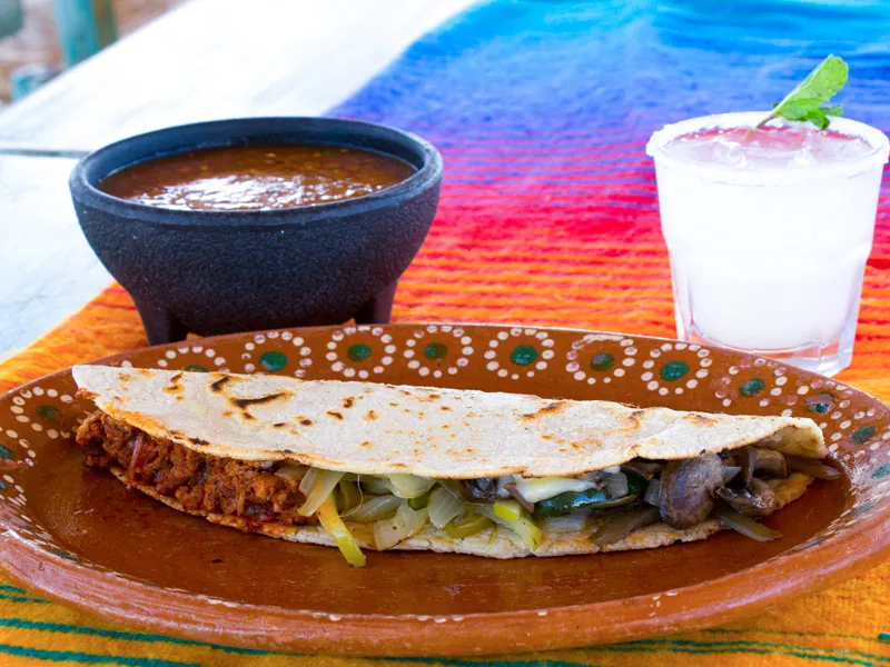 Quesadilla with salsa and a margarita on a colorful woven table runner