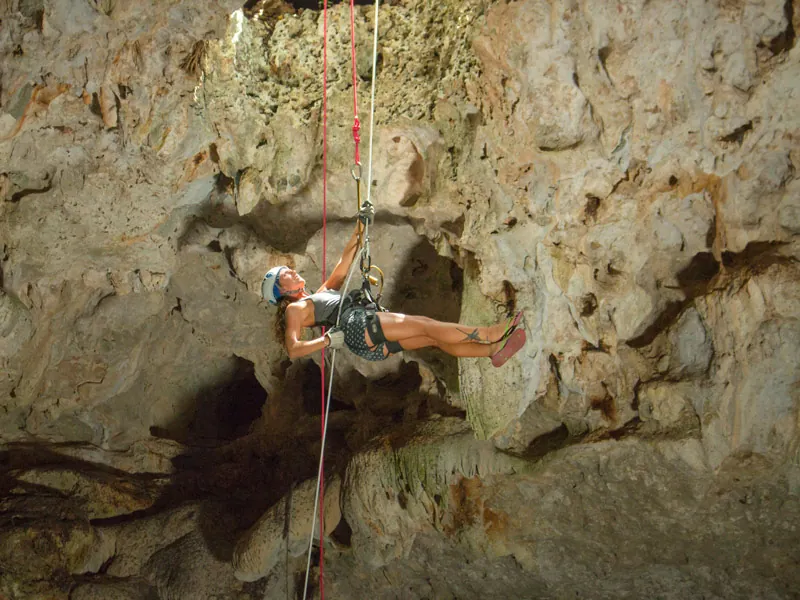 A woman in a harness and helmet rappelling down the rock wall of a cenote