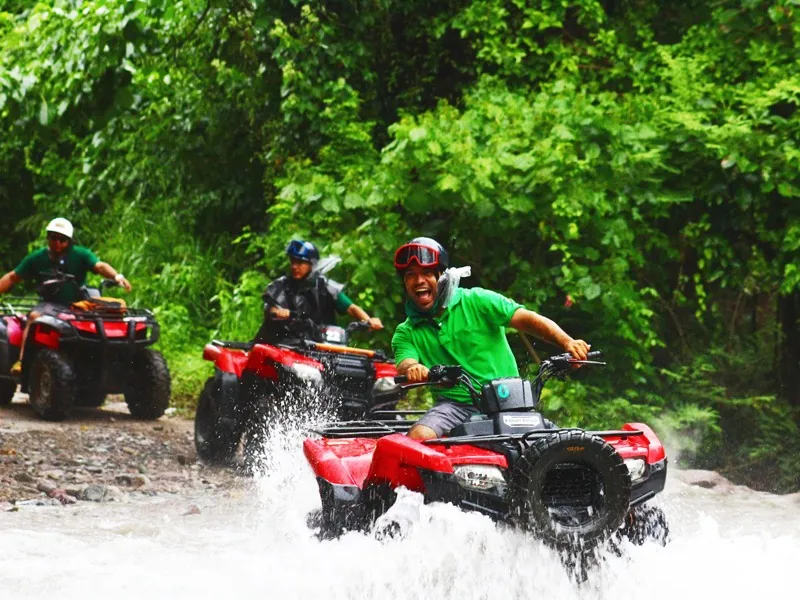 Three riders on red ATVs splashing through a shallow river in the jungle near Puerto Vallarta