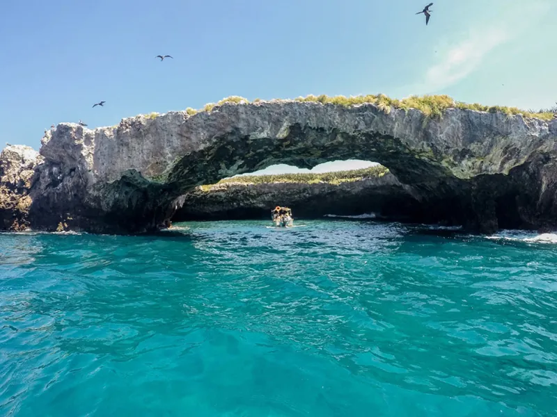 Natural rock arch at the Marietas Islands over turquoise water, frigatebirds overhead