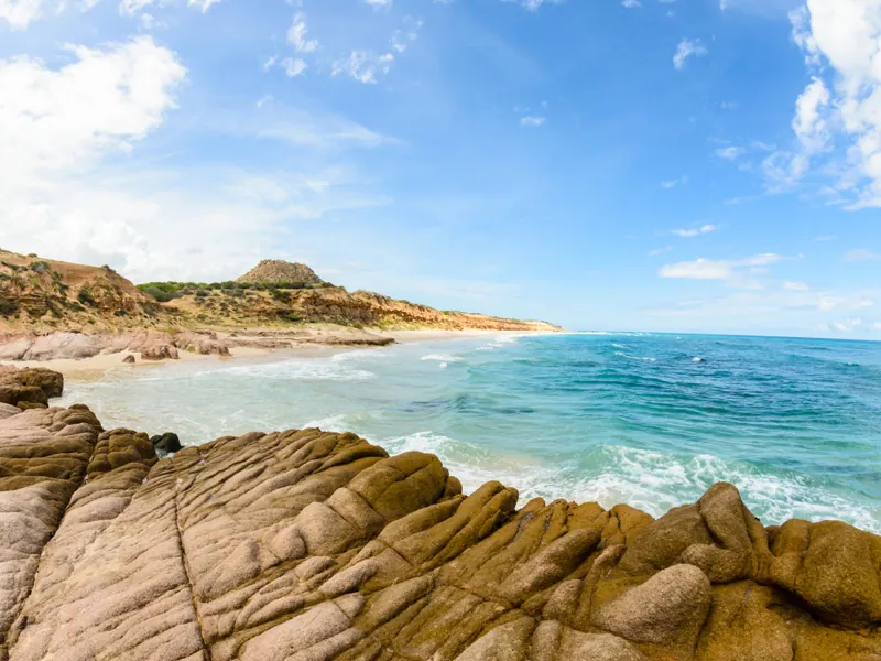 Weathered golden rocks in the foreground of a quiet beach and clear surf