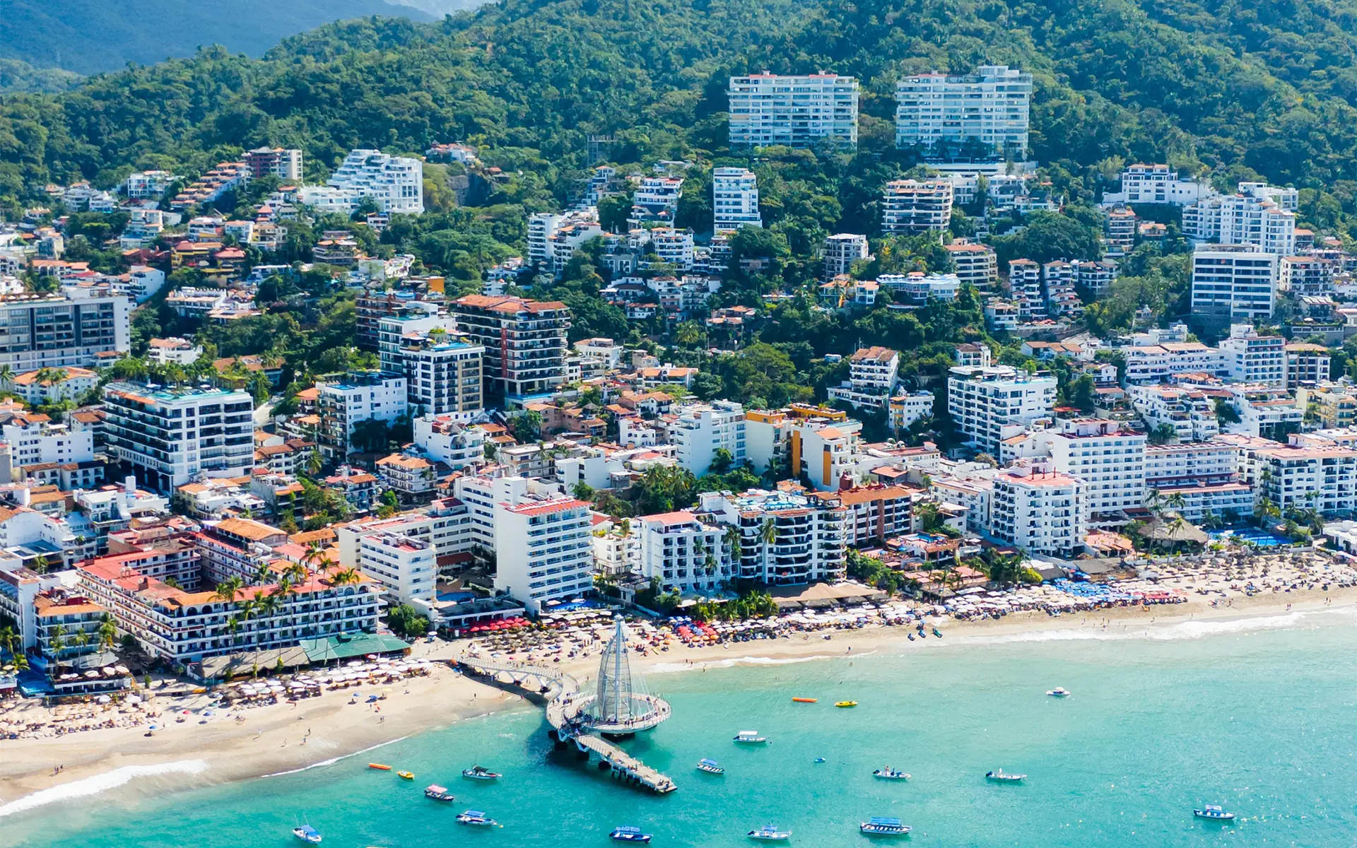 Aerial view of Puerto Vallarta’s Romantic Zone, Los Muertos pier and beach, with hillside homes and the Sierra Madre behind