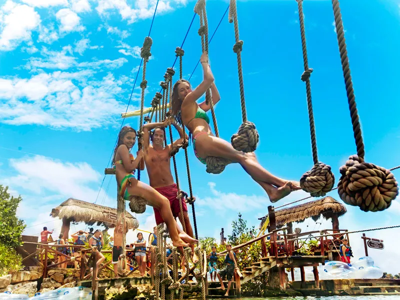 Three guests swing from knotted ropes over the water in the adventure area at Xel-Há