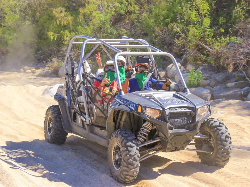 Guests in a Polaris RZR driving through a sandy desert wash
