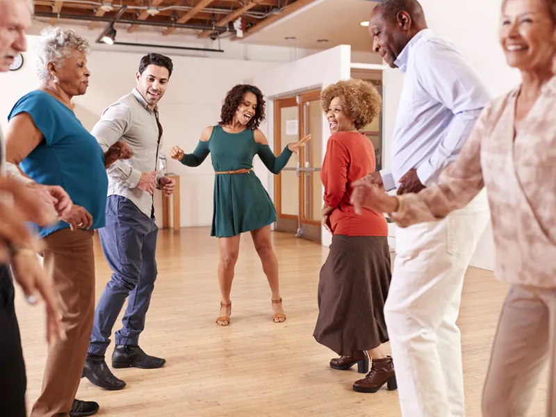 Group of adults dancing salsa in pairs in a bright wooden-floored room