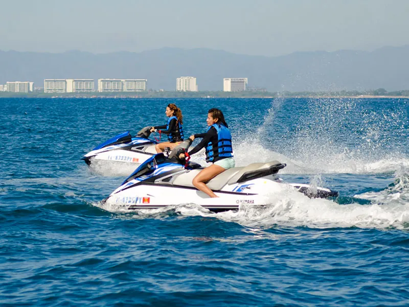 Two jet skis running side by side across the bay with the Puerto Vallarta skyline behind