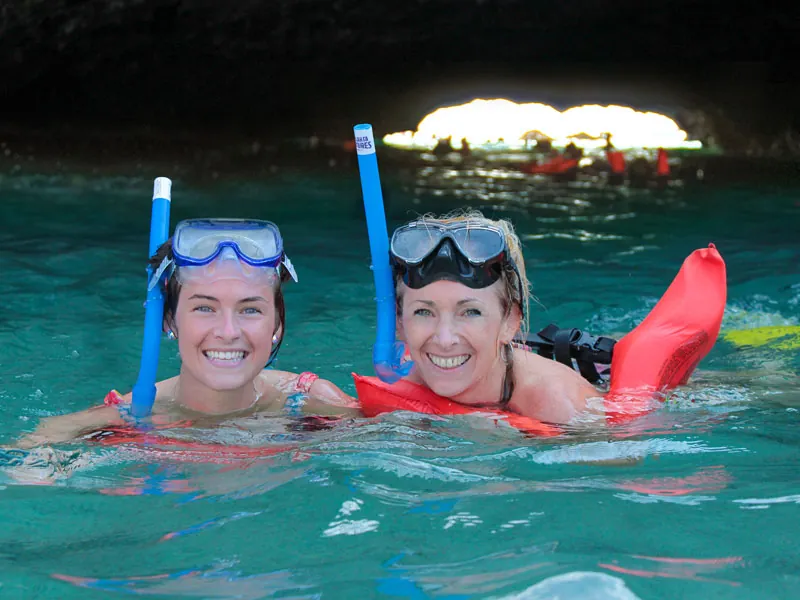 Two guests in snorkel masks smiling in a sea cave at the Marietas Islands, daylight at the cave mouth