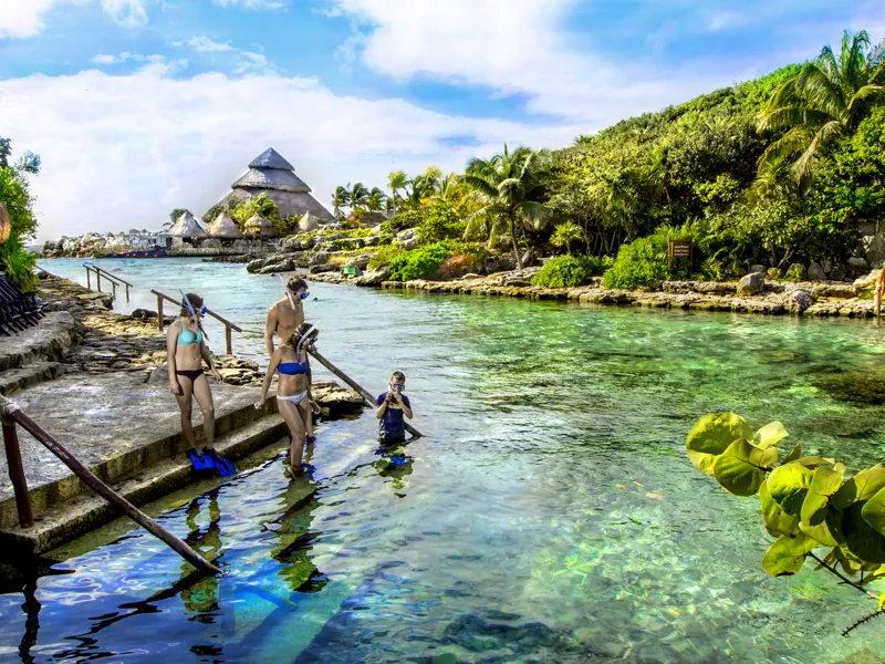 Snorkelers enter the clear water of an inlet at Xcaret from a stone jetty