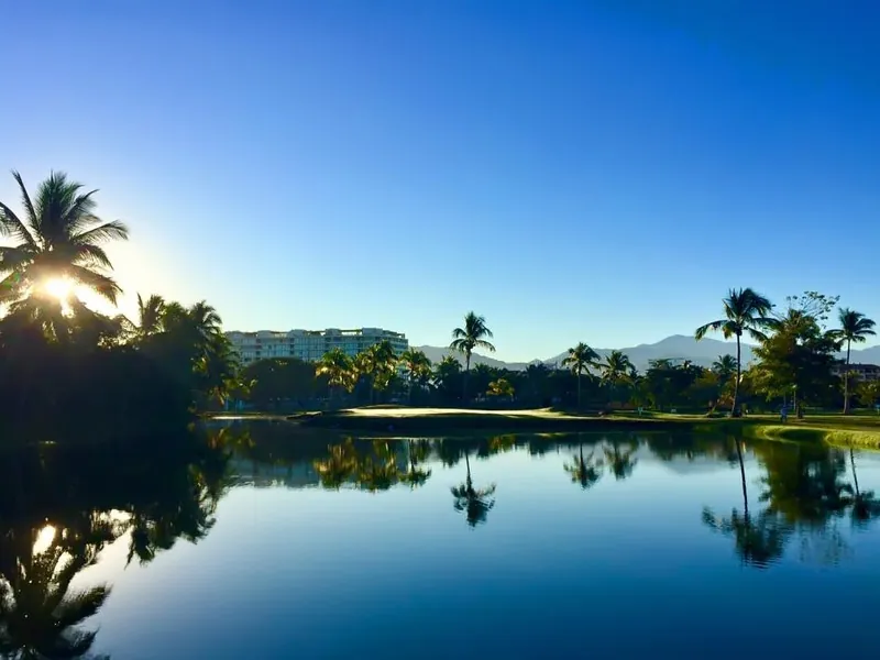 Sunrise over a still lagoon lined with palms on the course